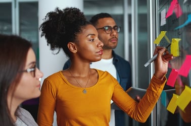 three people adding sticky notes to a planning board