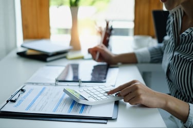 Close-up of a finance professional using a calculator while reviewing documents at a well-organized desk. The scene conveys a focused and professional approach to financial management.