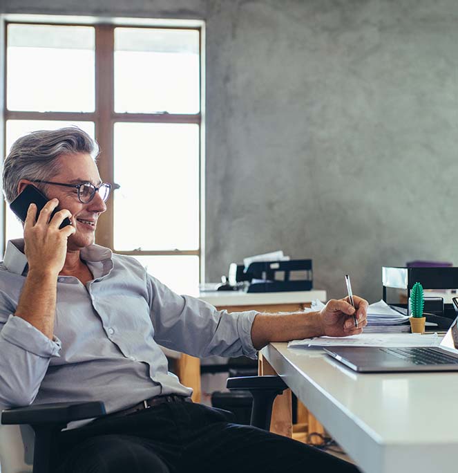 Man at a desk, on the phone, taking notes